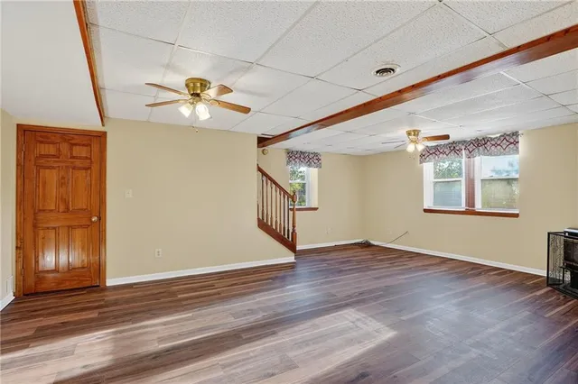 an empty room with wooden floor chandelier fan and windows
