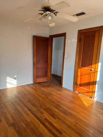 a view of an empty room with wooden floor and fan