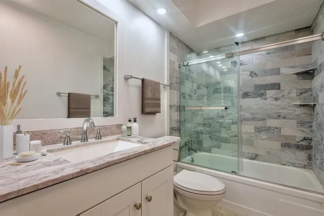 a bathroom with a granite countertop sink a toilet a mirror and shower