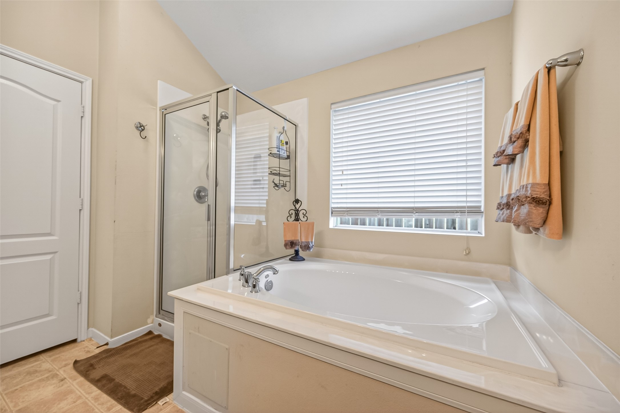 8622 Henrico Lane Rosenberg, TX 77469 - Photo 13 of 20 This bathroom features a spacious soaking tub with a modern glass-enclosed shower, neutral tile flooring, and a large window with blinds for natural light and privacy.