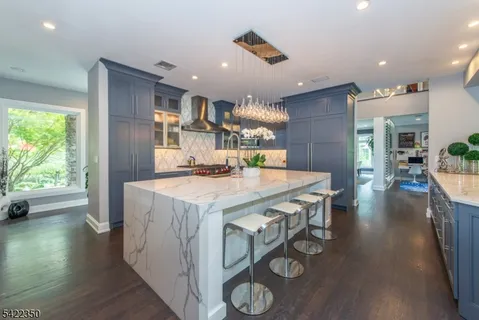 a open kitchen with stainless steel appliances granite countertop a refrigerator a oven a stove and a dining table with wooden floor
