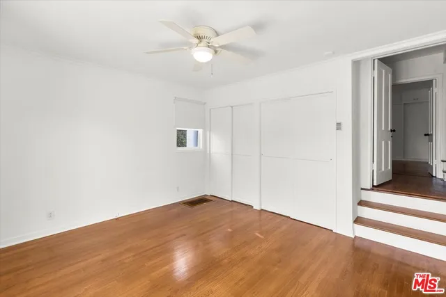 an empty room with wooden floor and fan