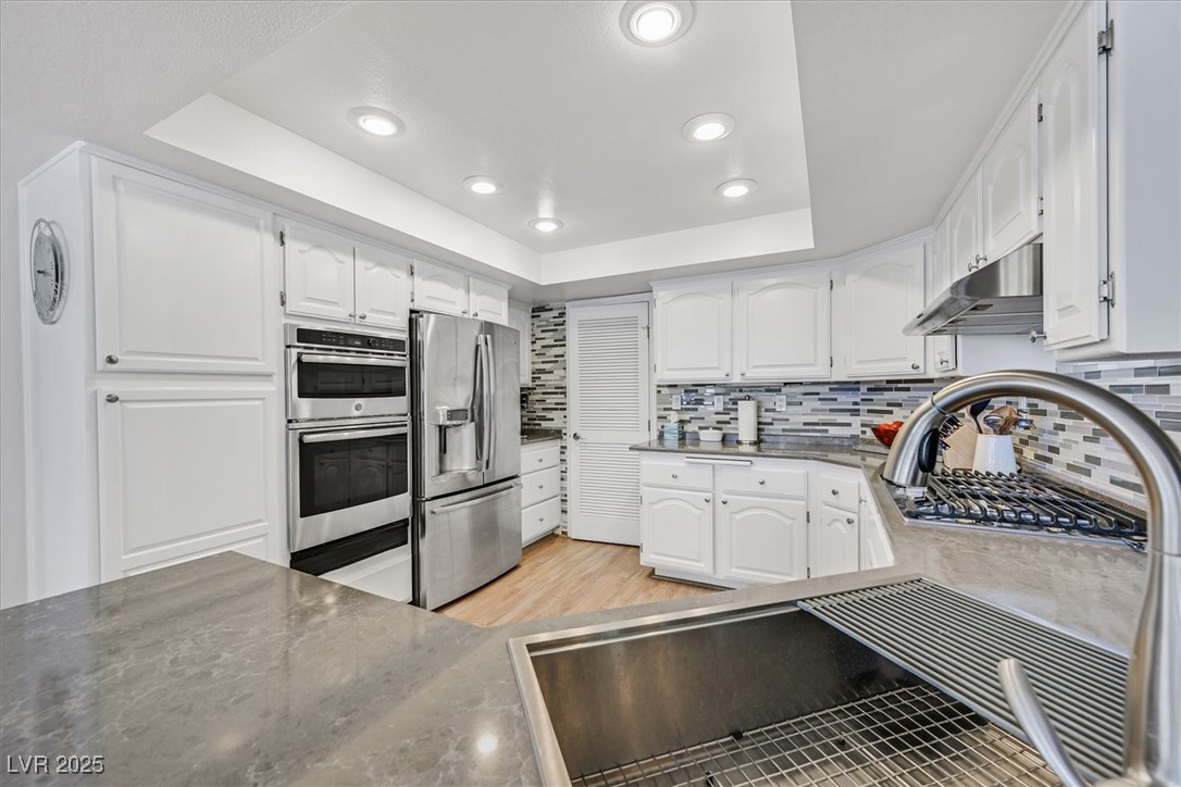18 Hummingbird Circle Henderson, NV 89014 - Photo 13 of 39 Kitchen with a raised ceiling, appliances with stainless steel finishes, white cabinets, tasteful backsplash, and recessed lighting