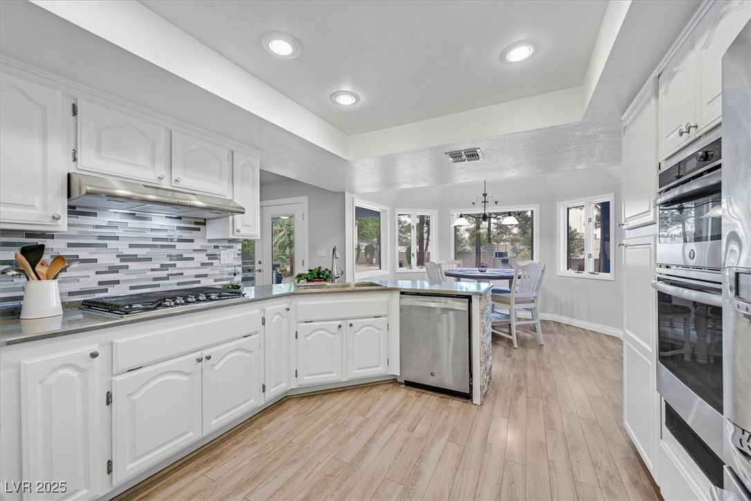18 Hummingbird Circle Henderson, NV 89014 - Photo 14 of 39 Kitchen with white cabinets, a raised ceiling, tasteful backsplash, a peninsula, and recessed lighting