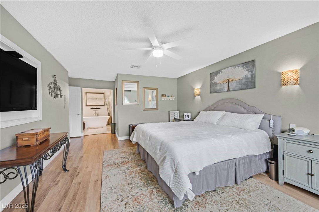 18 Hummingbird Circle Henderson, NV 89014 - Photo 19 of 39 Bedroom with light wood-style floors, ceiling fan, connected bathroom, and a textured ceiling