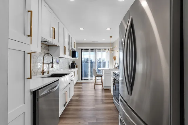 a kitchen with stainless steel appliances granite countertop a refrigerator a sink dishwasher a stove and white cabinets with wooden floor