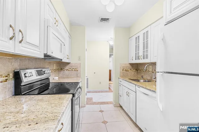 a kitchen with granite countertop a refrigerator sink stove and white cabinets