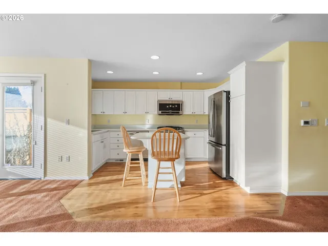 a kitchen with stainless steel appliances granite countertop a refrigerator a stove a sink dishwasher and a dining table with wooden floor