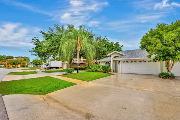 a view of white house with a big yard plants and palm trees