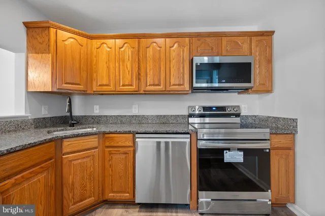 a kitchen with granite countertop wood cabinets stainless steel appliances and a sink
