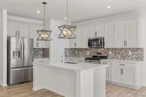 a kitchen with stainless steel appliances granite countertop a refrigerator a sink dishwasher a stove and white cabinets with wooden floor