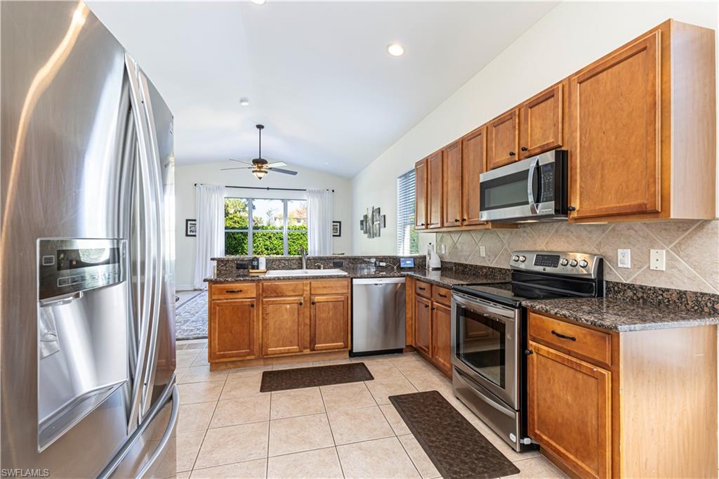 1767 Ribbon Fan Lane Naples, FL 34119 - Photo 6 of 31 Kitchen featuring kitchen peninsula, ceiling fan, stainless steel appliances, dark stone countertops, and vaulted ceiling