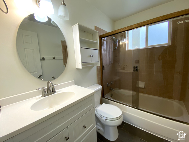 2989 Rae Street West Valley City, UT 84120 - Photo 10 of 25 Vanity with integrated sink and brushed nickel faucet, large oval mirror, built-in shelving, bath/shower combination with glass enclosure, and dark-toned floor tiling