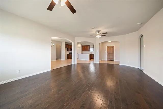 a view of an empty room with chandelier fan and wooden floor