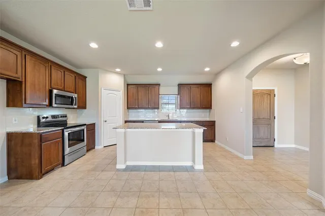 a large kitchen with stainless steel appliances granite countertop a stove top oven a sink and a refrigerator