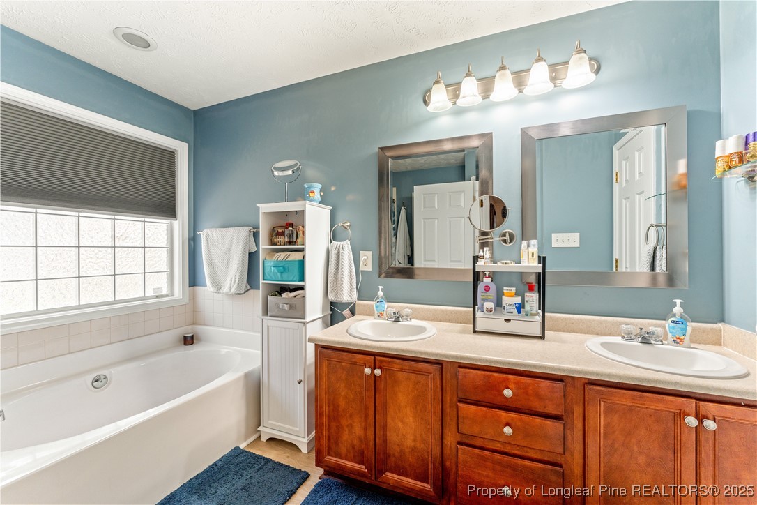 292 Falling Leaf Drive Raeford, NC 28376 - Photo 22 of 40 a bathroom with a tub a double vanity sink and a large mirror