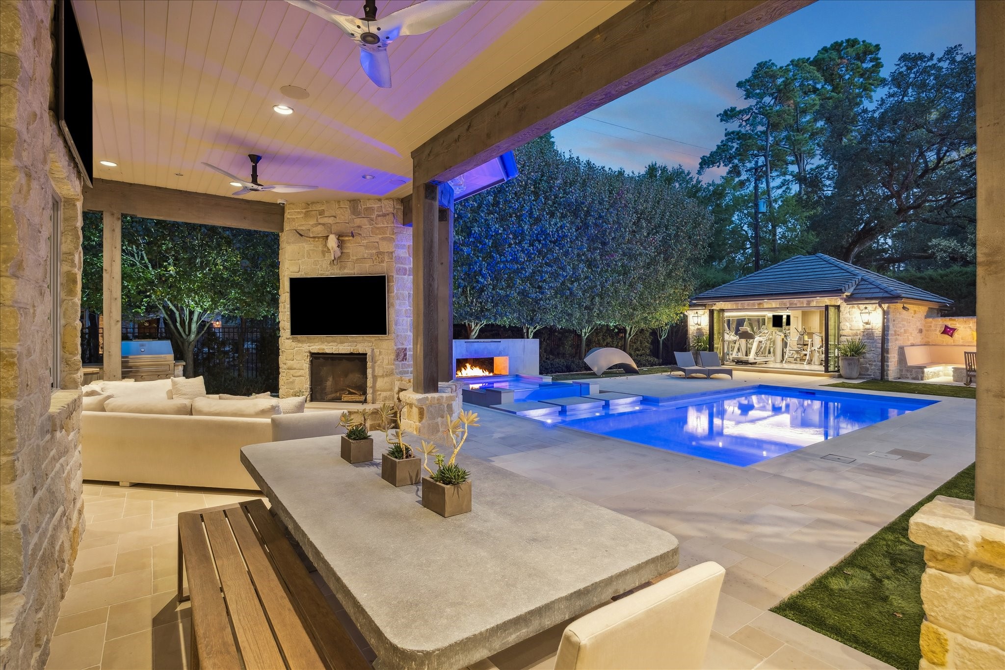 220 Merrie Way Lane Houston, TX 77024 - Photo 47 of 50 The backyard feels like a private resort, anchored by a shimmering pool and heated glass spa with a cascading water feature. Dual fire elements, a wood-burning fireplace, and a custom illuminated putting green bring both ambiance and personality to the space.