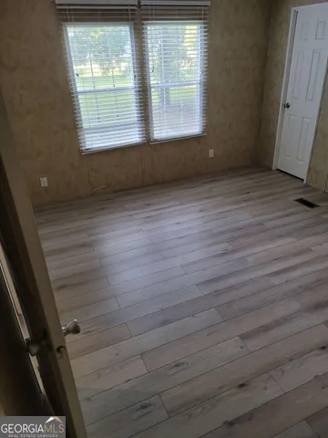 a view of an empty room with wooden floor and a window