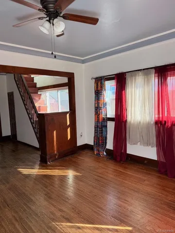 a view of an empty room with wooden floor and fan