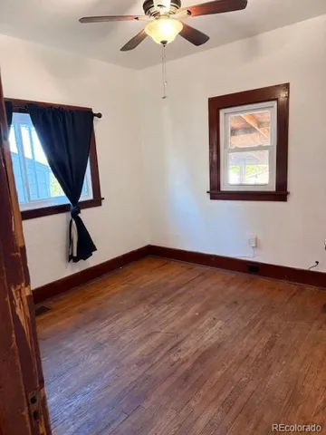 a view of an empty room with wooden floor and a ceiling fan