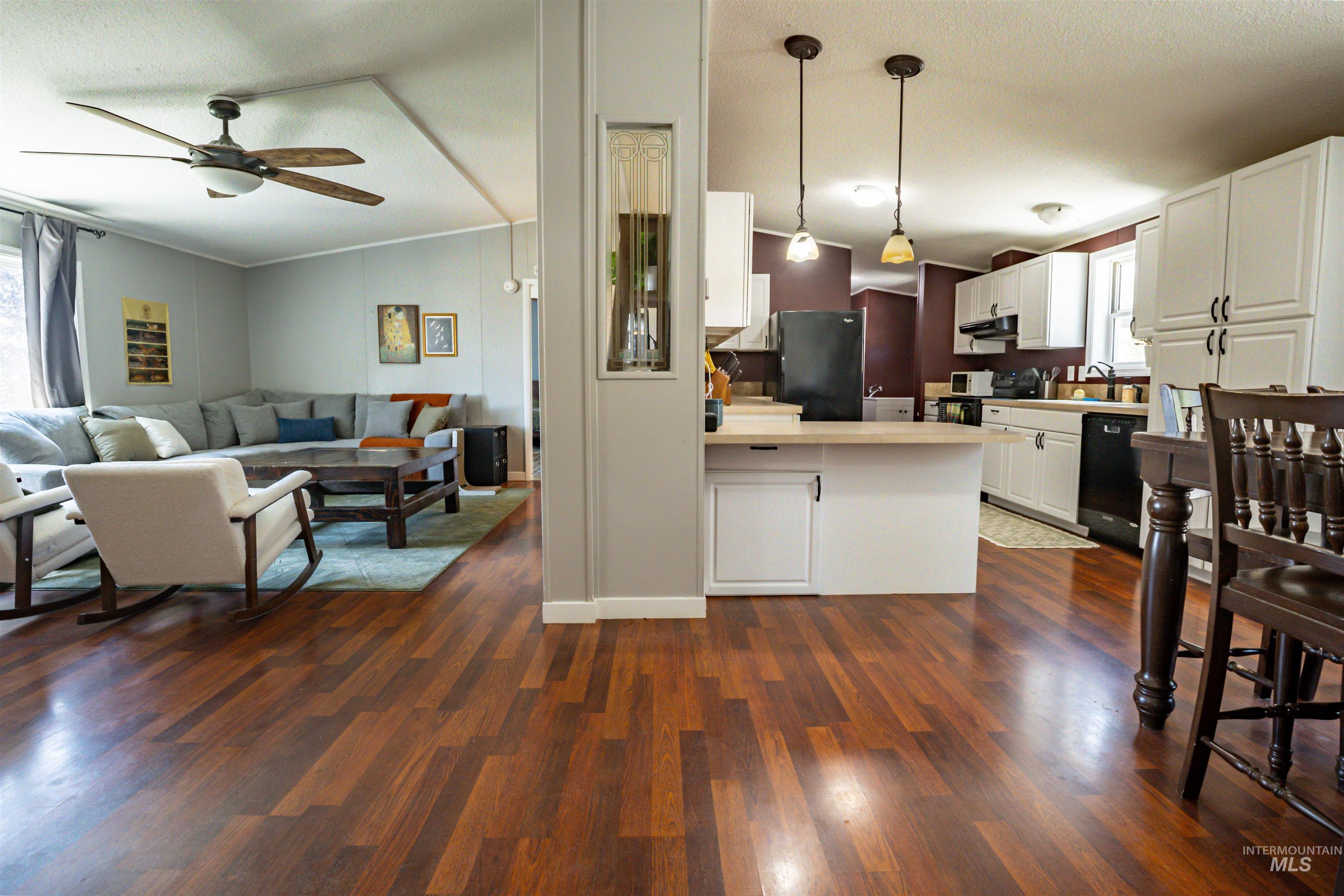 23904 Southview Lane Middleton, ID 83644 - Photo 22 of 29 Wood-finish flooring extending from the living area to the kitchen, featuring white cabinetry, a black appliance suite, a central island with pendant lighting, and a ceiling fan in the living space