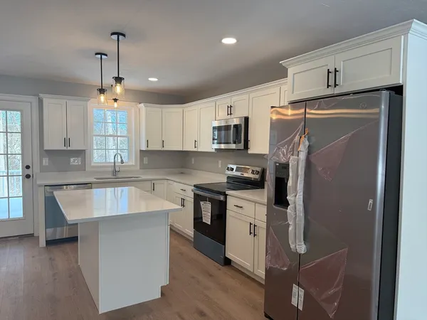 a kitchen with kitchen island granite countertop a refrigerator a sink dishwasher a stove and white cabinets with wooden floor