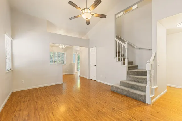 a view of an empty room with wooden floor and a ceiling fan
