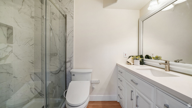 11128 South Barrett Pk Circle Sandy, UT 84092 - Photo 25 of 36 Bathroom featuring a glass-enclosed shower with tiled walls and a recessed niche, a white vanity with an integrated sink, a large framed mirror, and wood-finish flooring