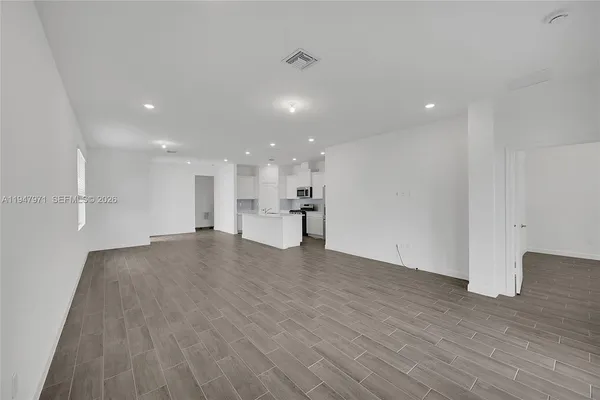 a view of empty room with wooden floor and kitchen