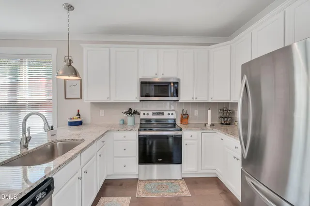 a kitchen with stainless steel appliances granite countertop a refrigerator stove a sink and white cabinets