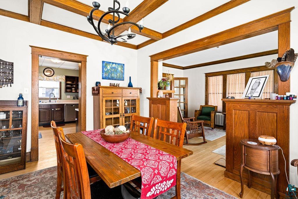 23 5th Street Proctor, MN 55810 - Photo 11 of 32 Dining space featuring beamed ceiling, radiator, sink, a chandelier, and light wood-type flooring