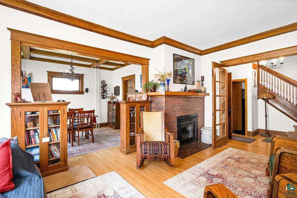 23 5th Street Proctor, MN 55810 - Photo 10 of 32 Living room featuring beamed ceiling, a fireplace, a notable chandelier, ornamental molding, and light wood-type flooring