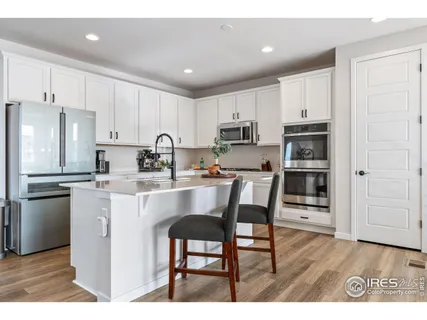 a kitchen with stainless steel appliances granite countertop a refrigerator a stove a sink and white cabinets with wooden floor