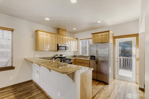 a kitchen with stainless steel appliances granite countertop a refrigerator a stove and a sink with wooden floor