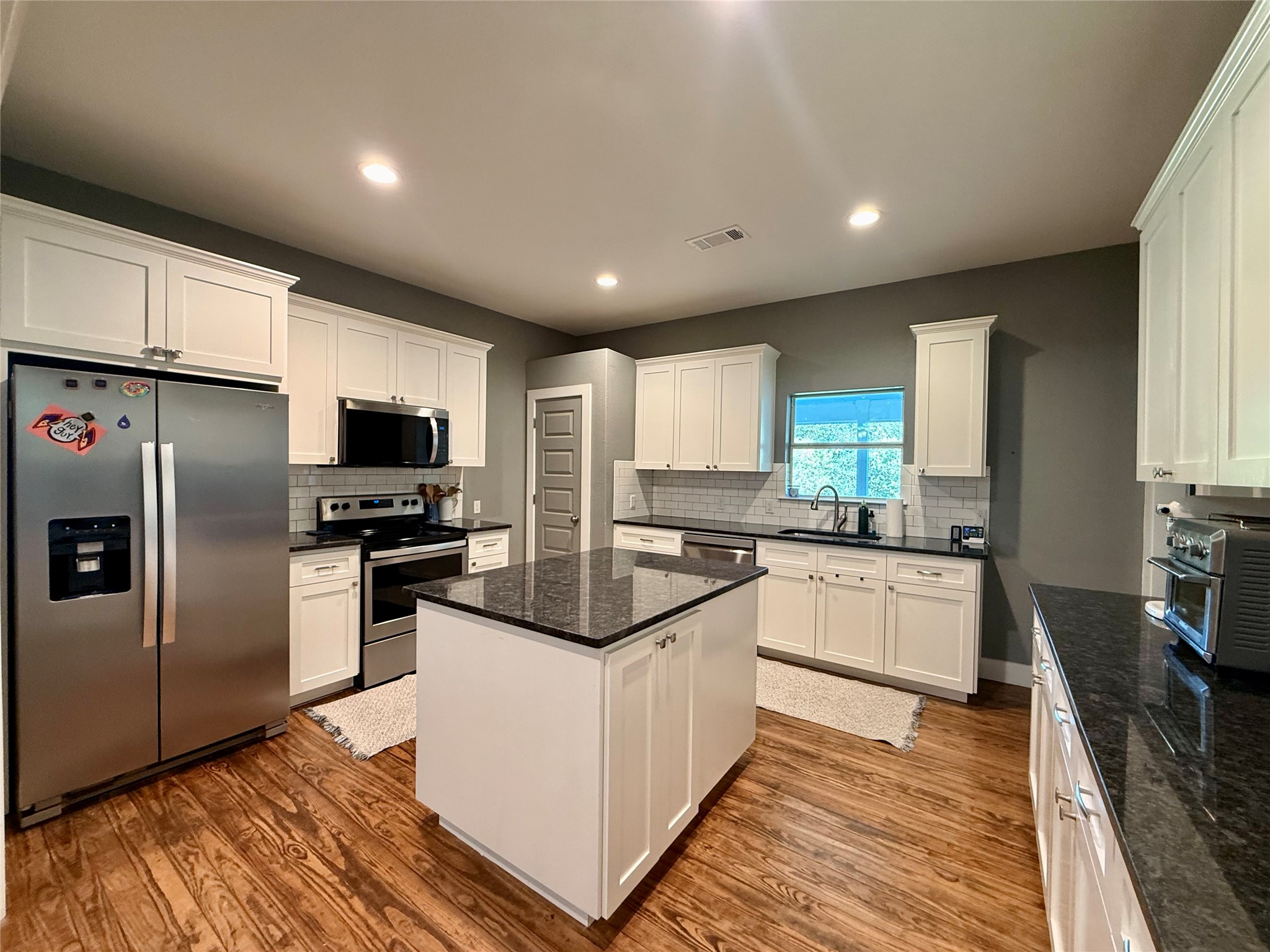 739 Pleasant Grove Road Elgin, TX 78621 - Photo 8 of 29 Modern kitchen featuring wood-finish flooring, white cabinetry, dark countertops, a tile backsplash, and recessed lighting