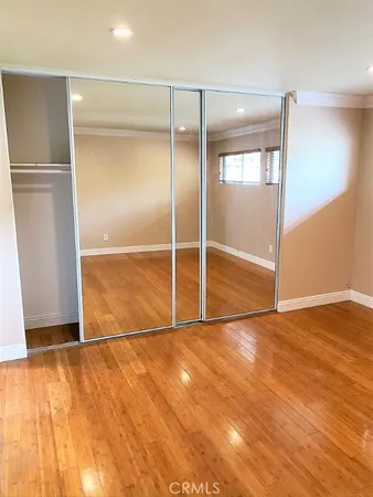 a view of an empty room with wooden floor and a kitchen