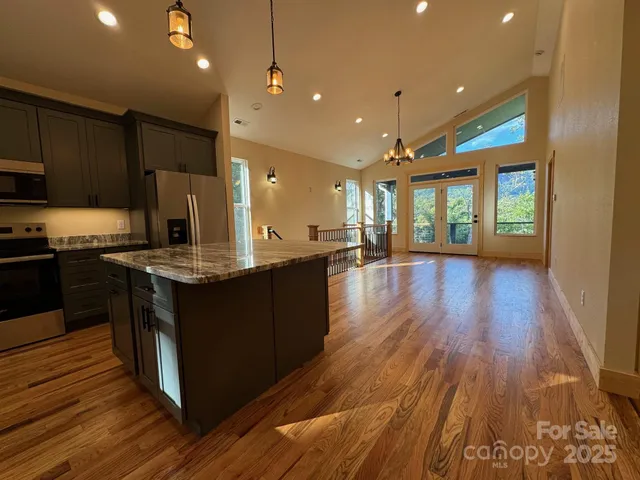 a kitchen with stainless steel appliances granite countertop a stove a sink a refrigerator and a oven with wooden floor