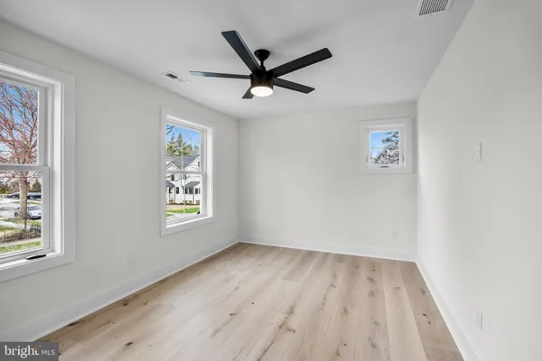 an empty room with wooden floor a ceiling fan and windows