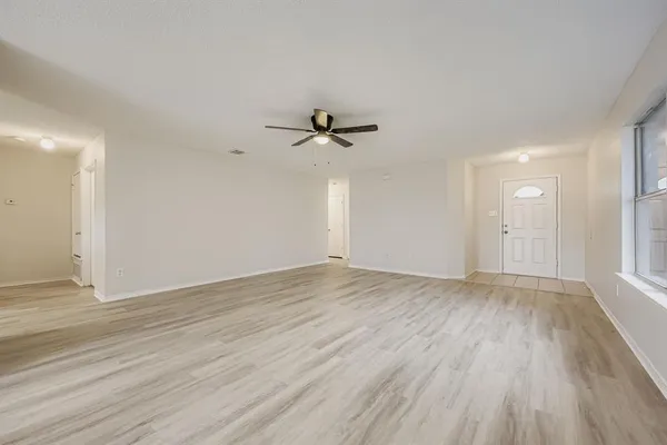 an empty room with wooden floor fan and windows