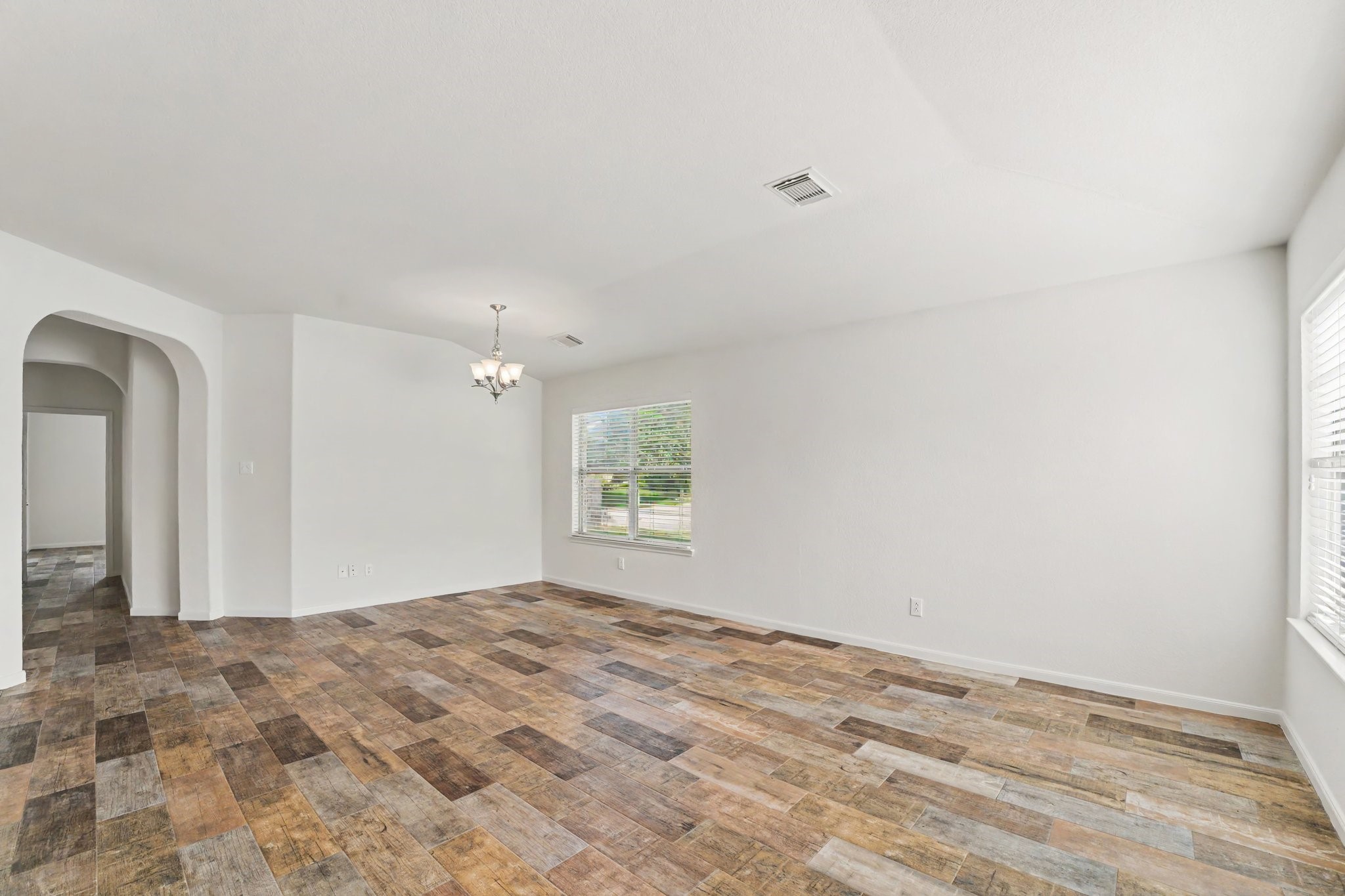 21427 Blooming Rock Lane Spring, TX 77379 - Photo 3 of 32 The photo showcases a spacious, bright room with neutral walls and wood-look tile flooring. It features a charming arched doorway, large windows for natural light, and a modern ceiling light fixture. Perfect for a living or dining area.
