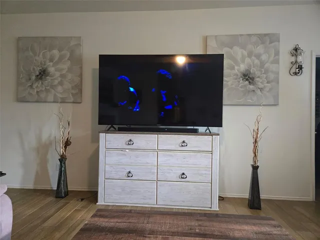 a living room with flat screen tv on a dresser and a wooden floor