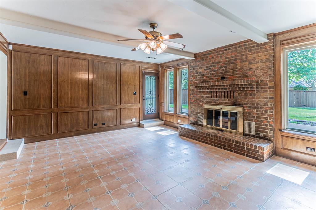 127 Nicklaus Nook Lancaster, TX 75146 - Photo 5 of 37 Unfurnished living room with a ceiling fan, wood walls, a fireplace, beam ceiling, and light tile patterned flooring