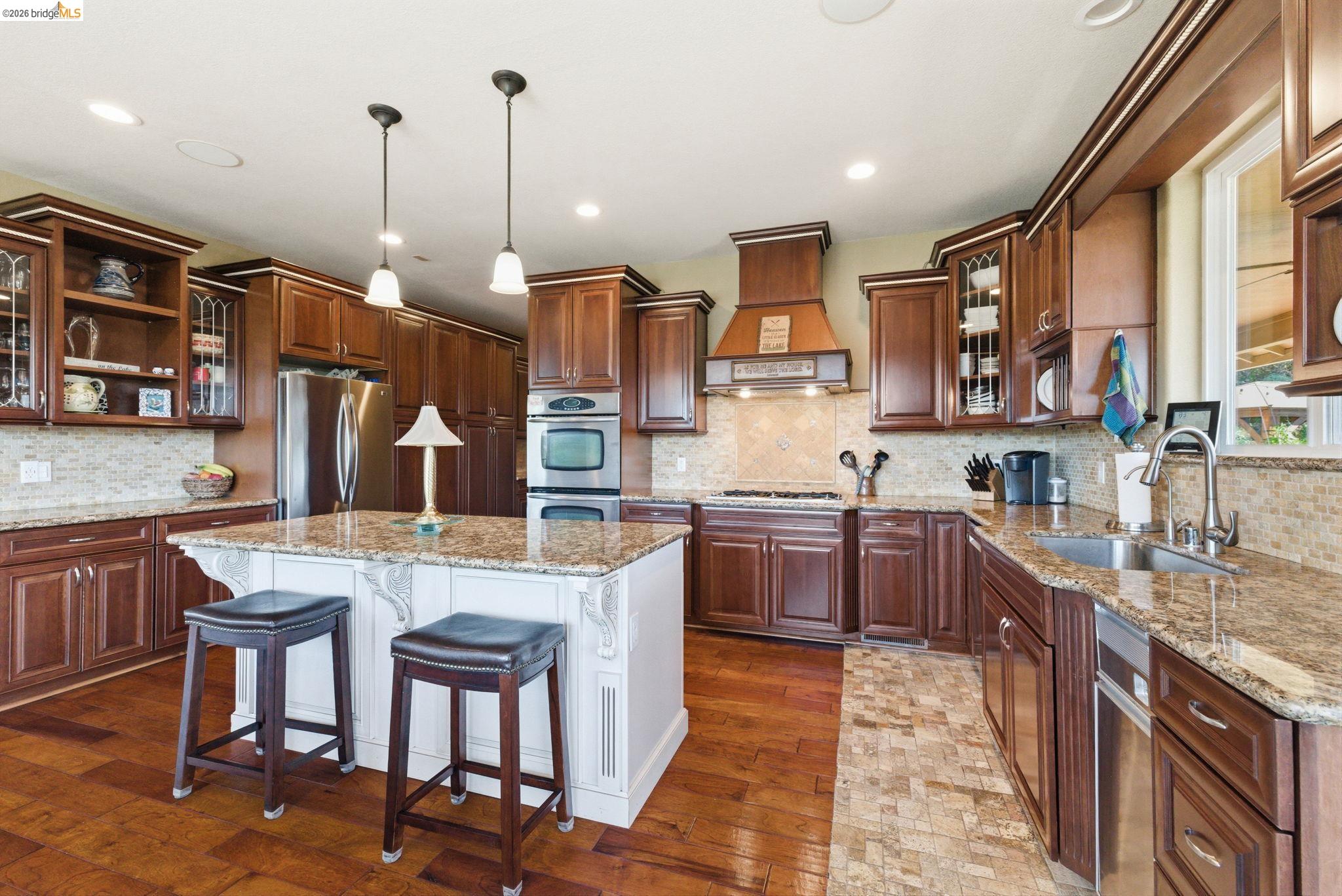 12808 Mammoth Mine Road Jamestown, CA 95327 - Photo 16 of 60 Two tone kitchen featuring glass fronted cabinets, a kitchen breakfast bar, light stone countertops, a center island, and stainless steel appliances
