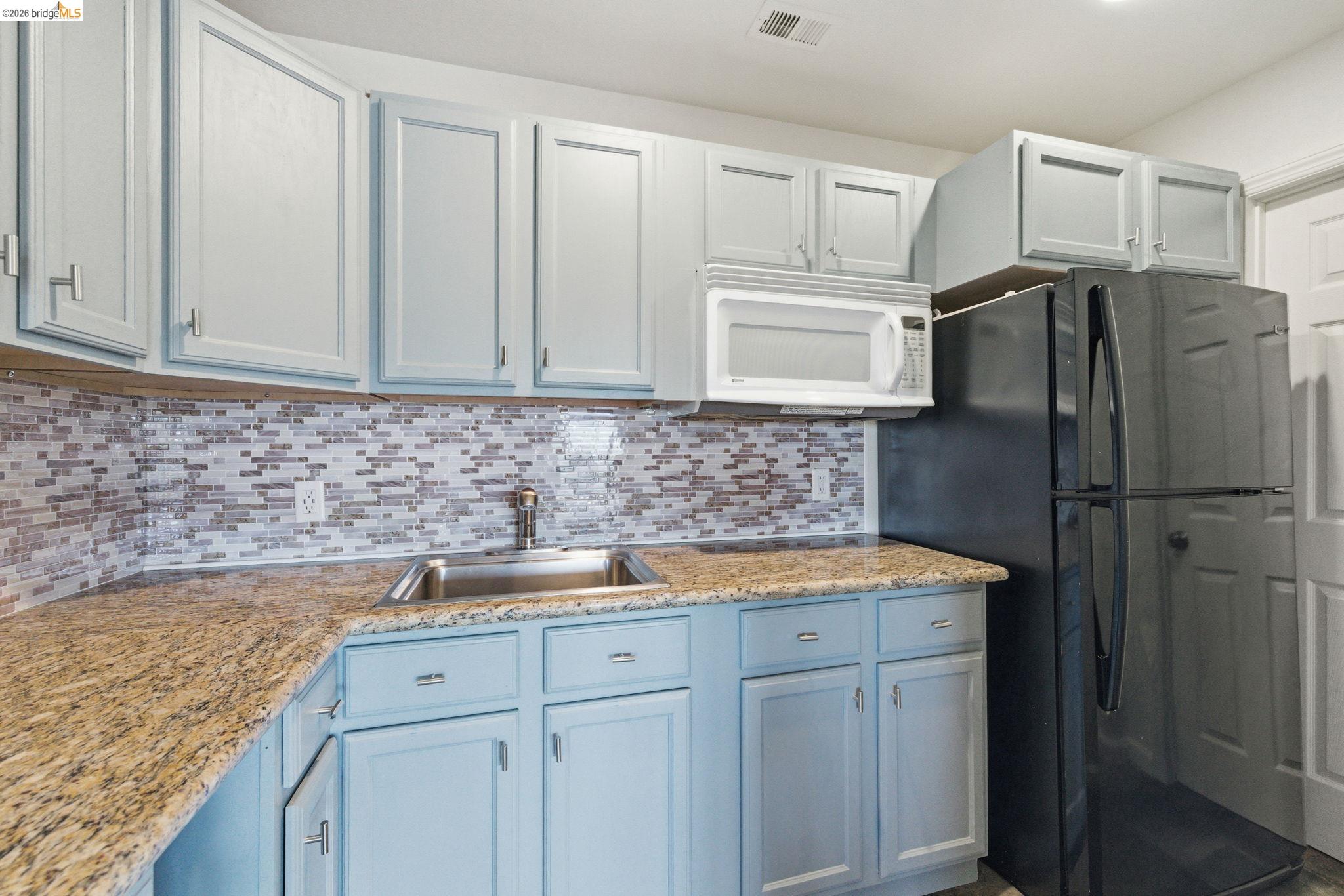 12808 Mammoth Mine Road Jamestown, CA 95327 - Photo 30 of 60 Kitchen with freestanding refrigerator, white microwave, light stone countertops, decorative backsplash, and white cabinetry