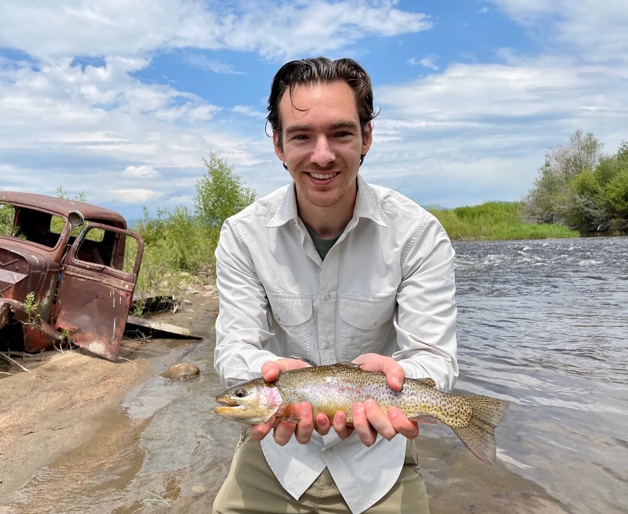 Man holding fish next to stream with old truck