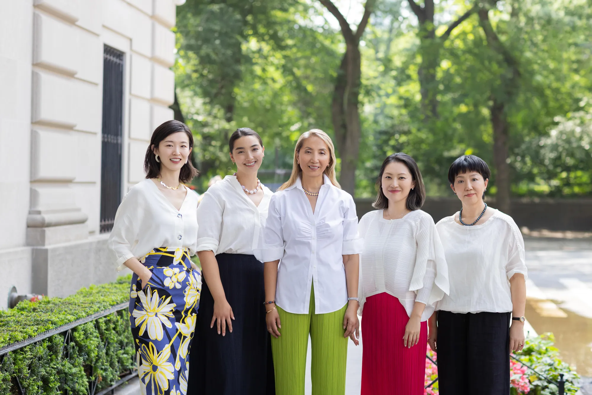 The Jing Chen Team, comprised of 5 women, standing in a row wearing white blouses with trees and a limestone building in the background.