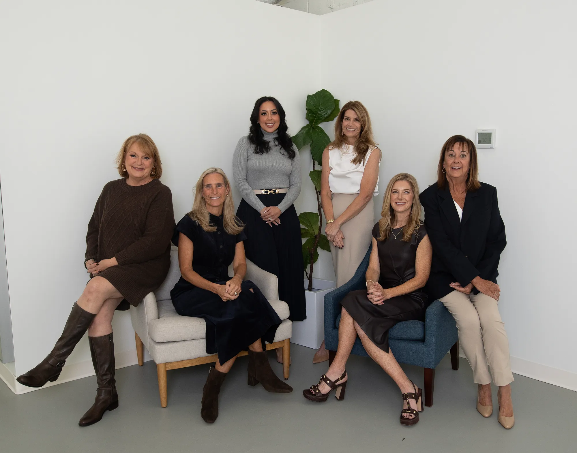 The Jen Holden Group team of six women, seated and standing together in a bright studio, smiling at the camera.