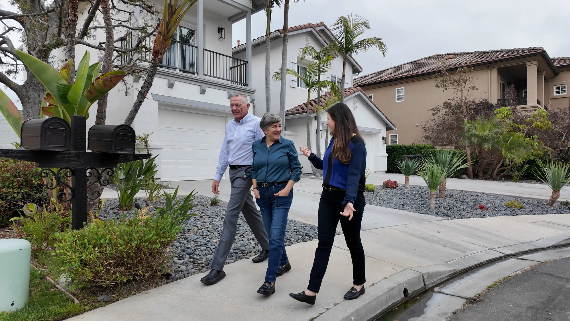 An image of real estate agents Doug, Soosan, and Serena wearing business professional attire walking in a community with a home behind them.