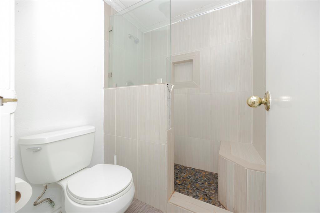 18333 Roehampton Drive, Unit 825 Dallas, TX 75252 - Photo 9 of 23 Glass-enclosed shower with a built-in bench, tiled walls, and a pebble-finish floor