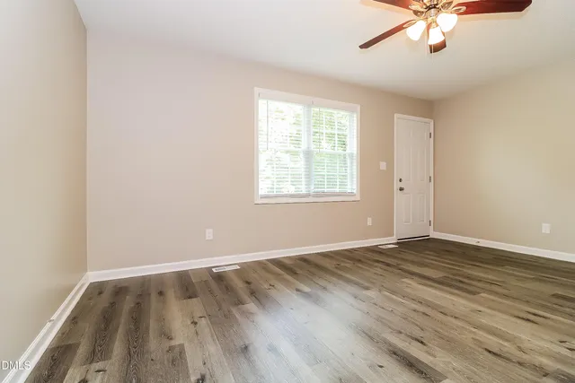 an empty room with wooden floor chandelier fan and windows